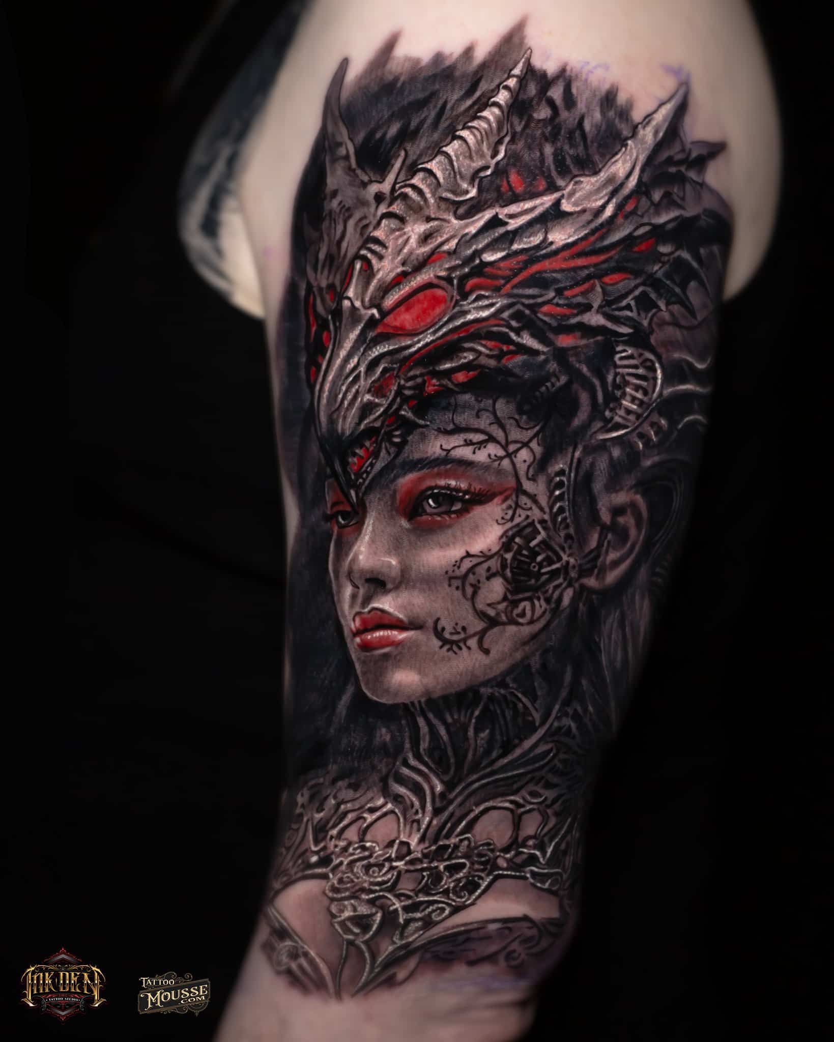 Tattoo of a dark fantasy woman’s face with red eyes and ornate black-red headdress on an arm