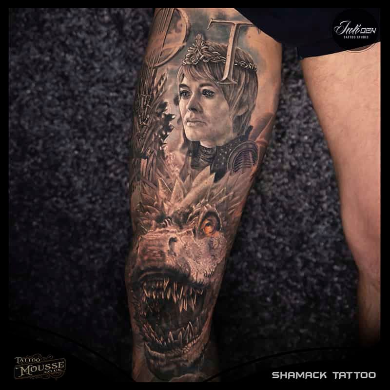 Dark grayscale tattoo on an arm featuring a woman’s portrait and snarling monster face