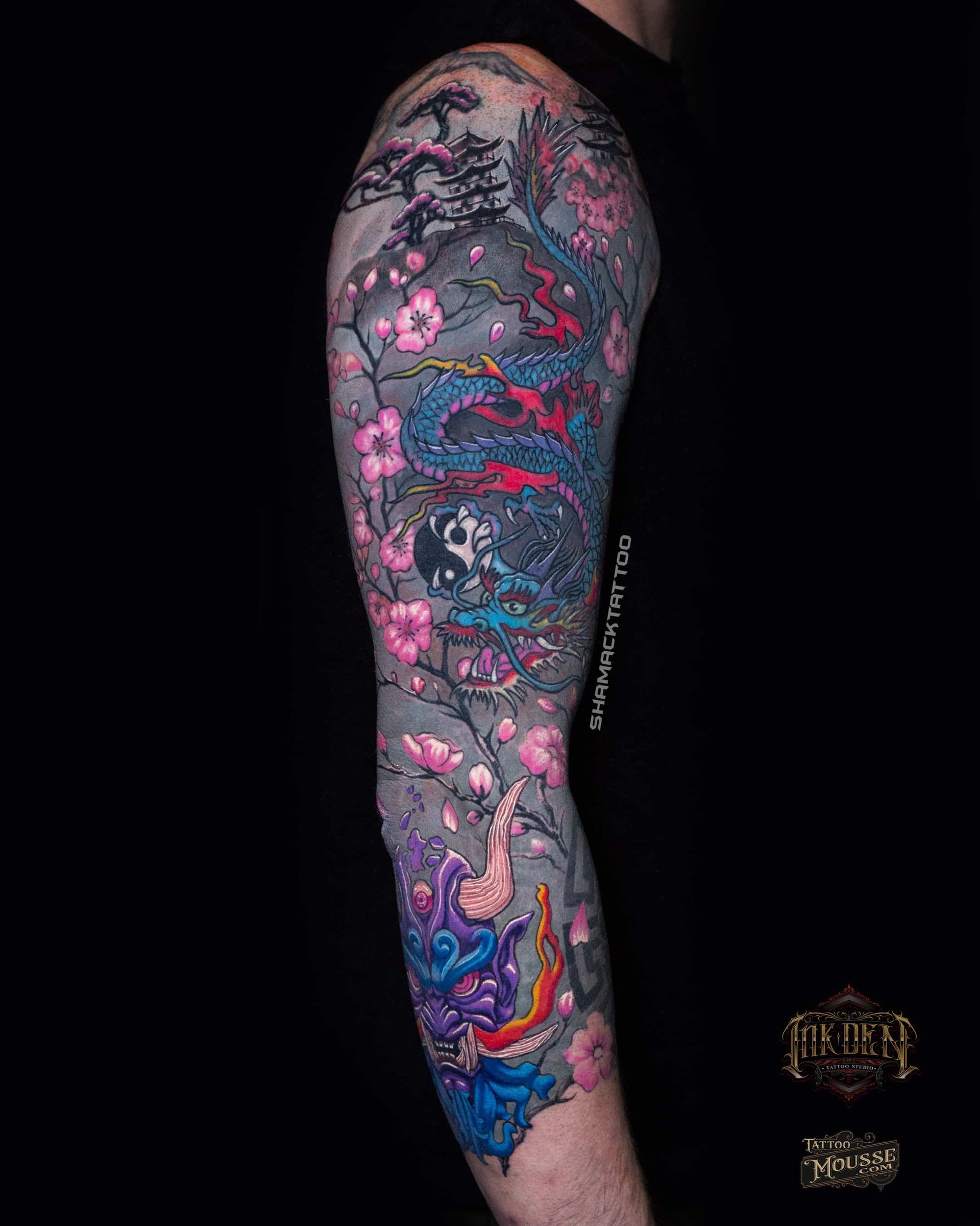 Tattooed arm in side view, covered in colorful floral and abstract sleeve art on black background