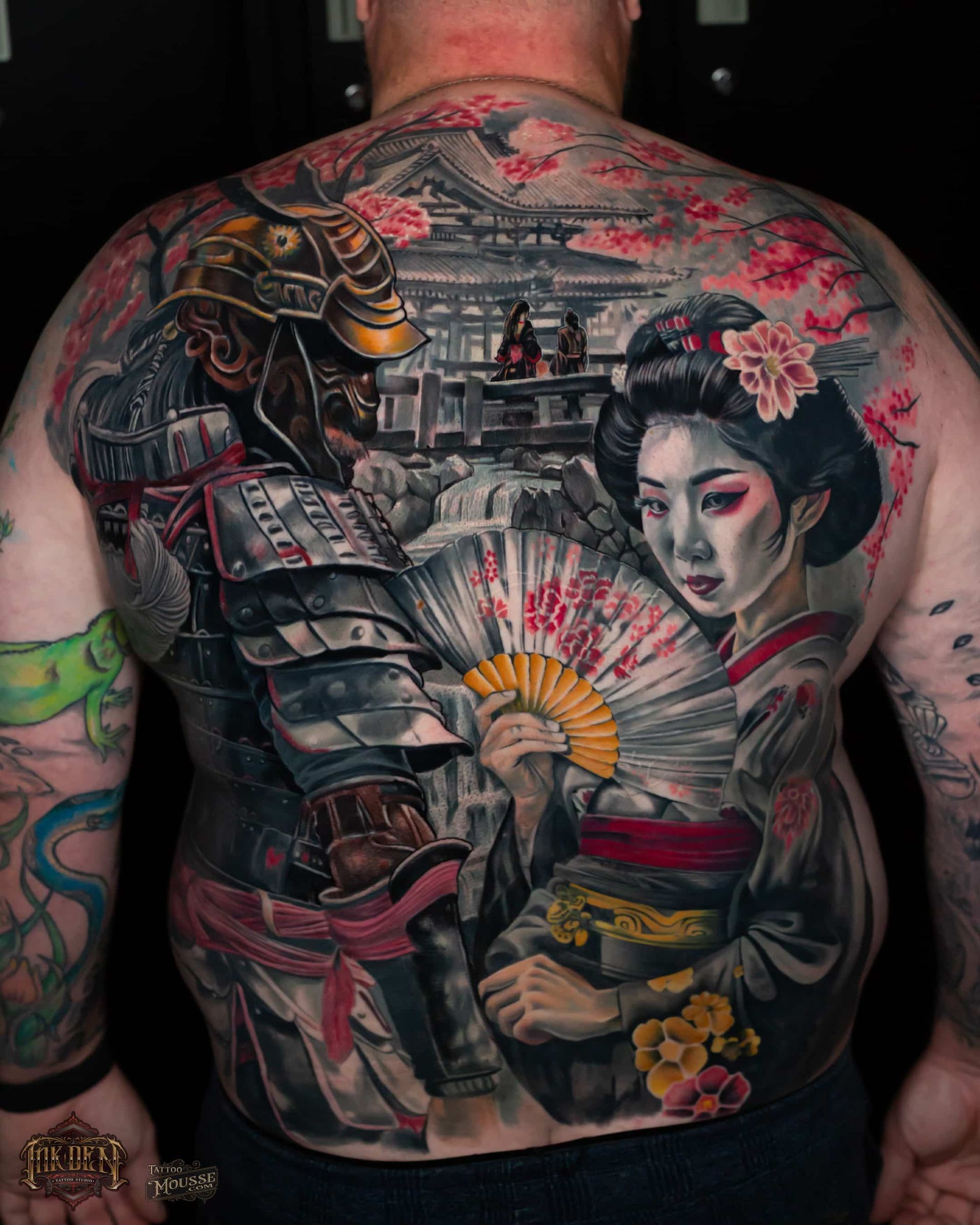 Back tattoo of a Japanese warrior and geisha with cherry blossoms, fan, and temple scene in vivid red and black
