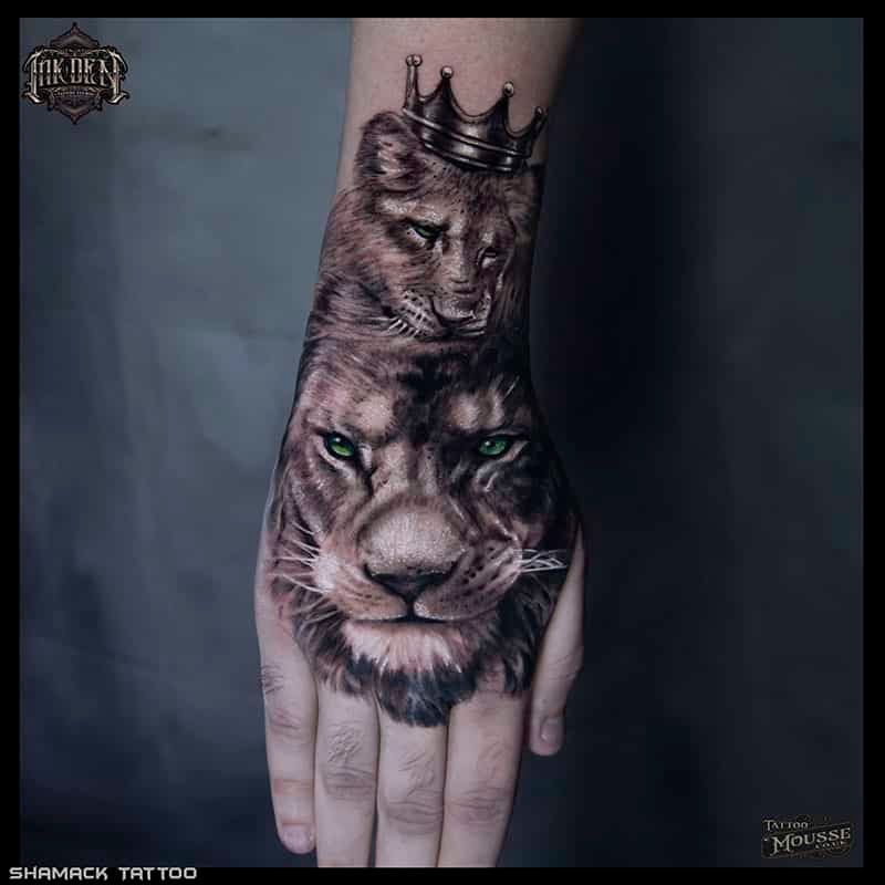 Tattooed hand with a crowned lion face over a cat’s face on the forearm