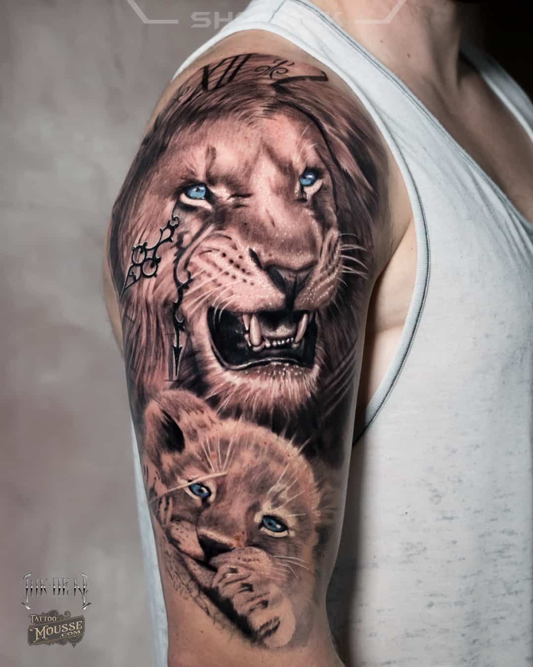 Arm tattoo of two realistic lion faces, one roaring with blue eyes and the other calm, on a person’s upper arm