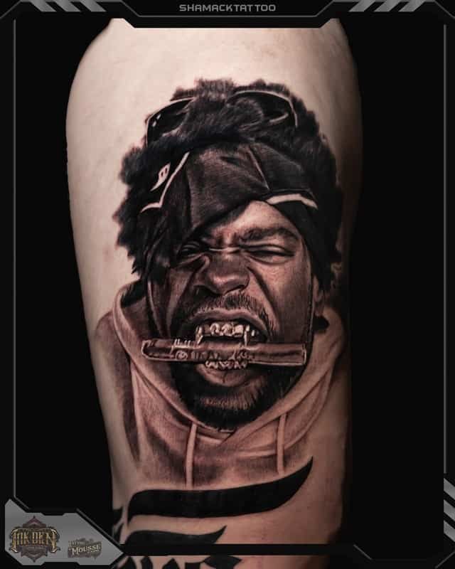 Black-and-gray tattoo of a snarling face with a bar through the mouth on a forearm