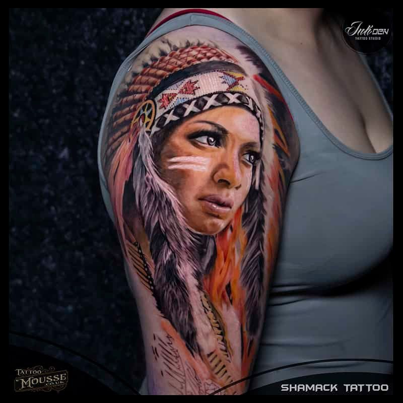 Colorful tattoo portrait of a woman in a feathered headdress on an upper arm