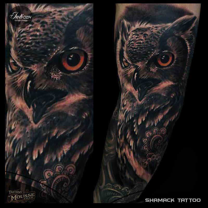 Black-and-gray owl tattoo sleeve with vivid orange eyes on a forearm