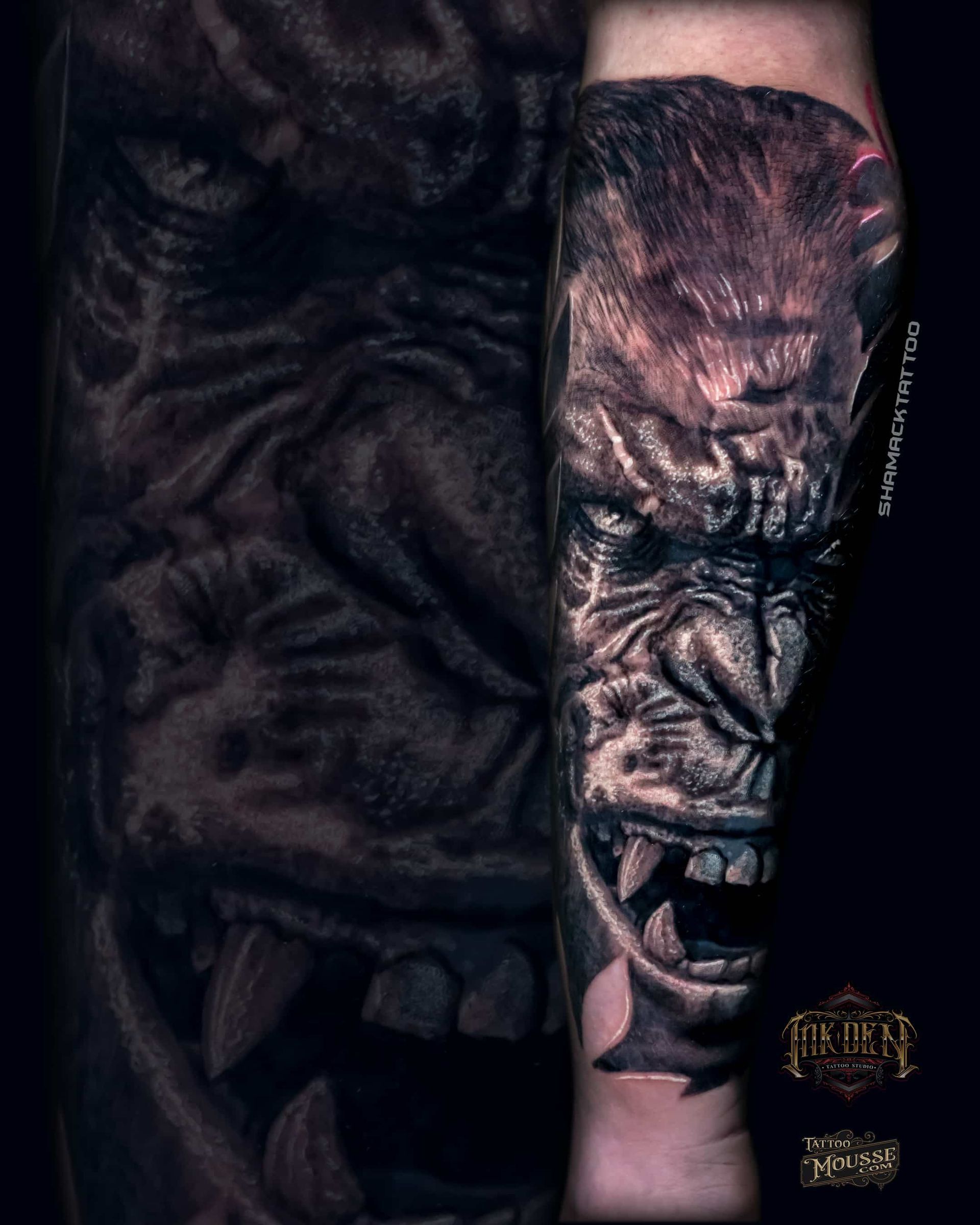 Close-up of a dark tattooed torso and forearm with a detailed black-and-gray portrait tattoo.