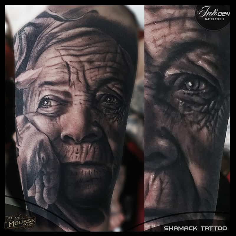 Tattoo close-up of a wrinkled elderly face in black and gray ink, split into two detailed portraits
