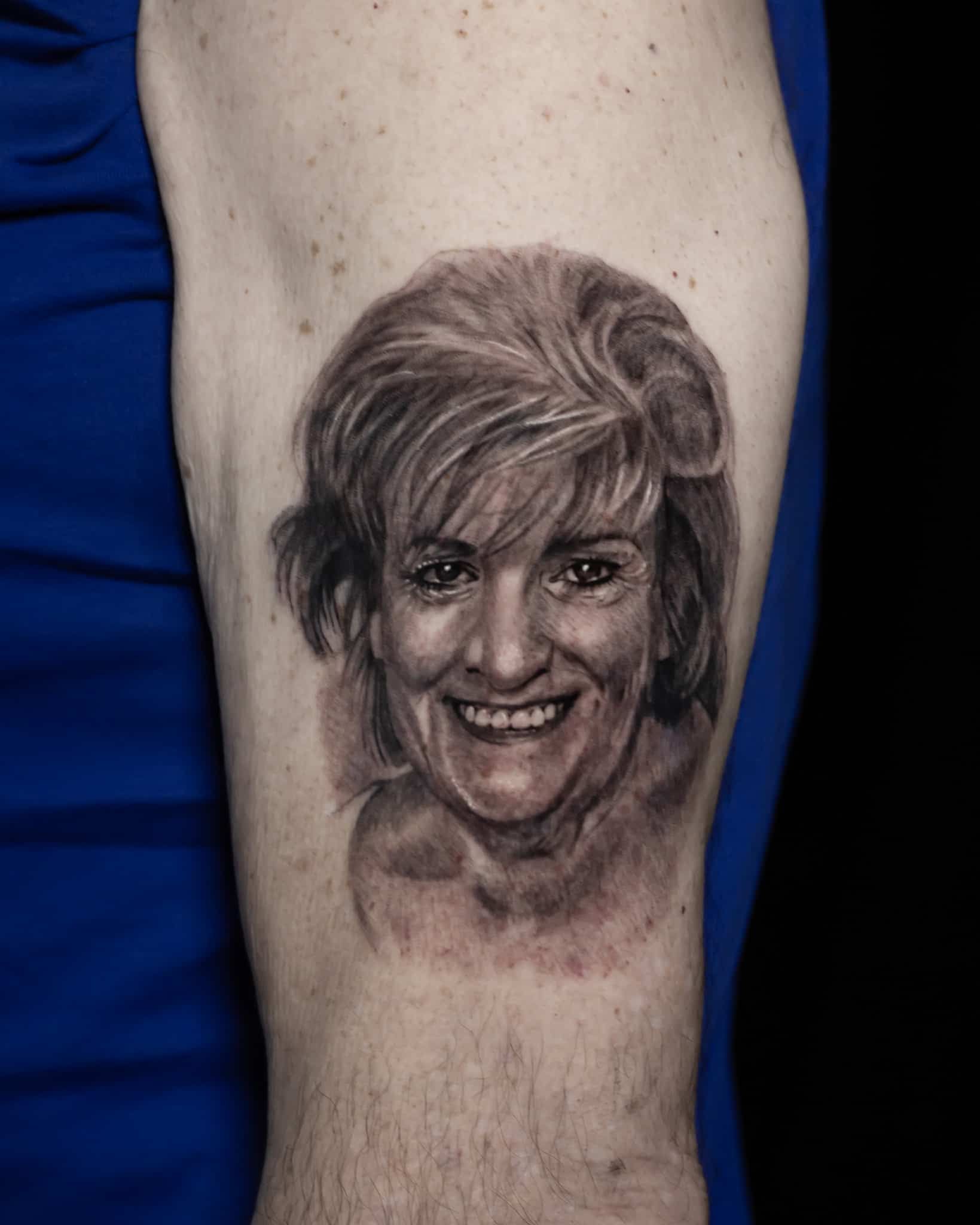 Tattoo portrait on a forearm of a smiling woman's face in black and gray ink