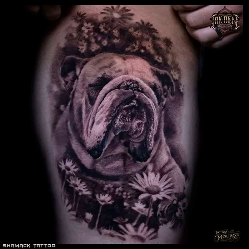 Black-and-gray bulldog tattoo surrounded by flowers on a person’s skin