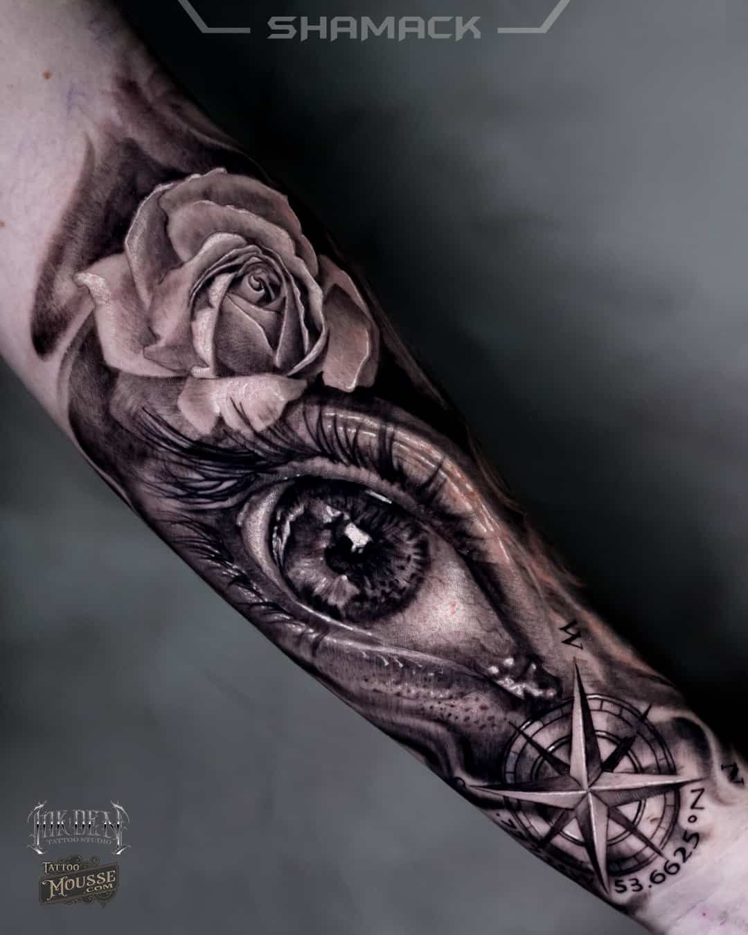 Black-and-gray forearm tattoo of a realistic eye, rose, and geometric compass design