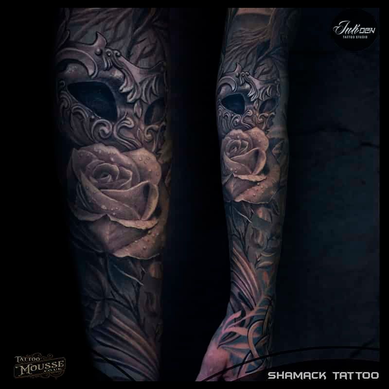 Black-and-gray forearm tattoo with roses, leaves, and a skull motif on a dark background