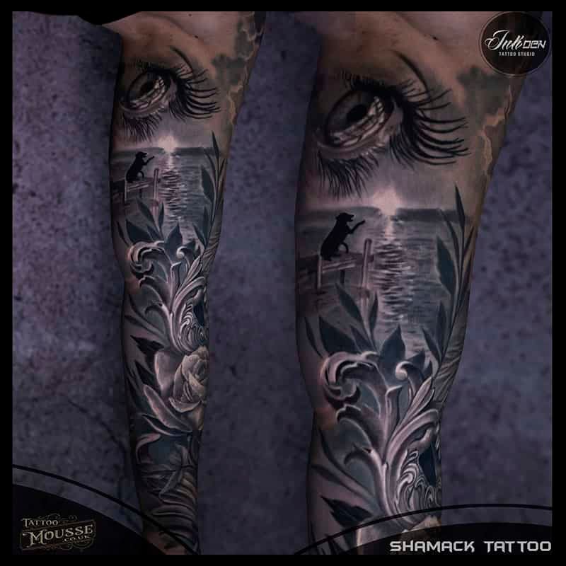 Close-up of two tattooed lower legs with black-and-gray floral and landscape designs