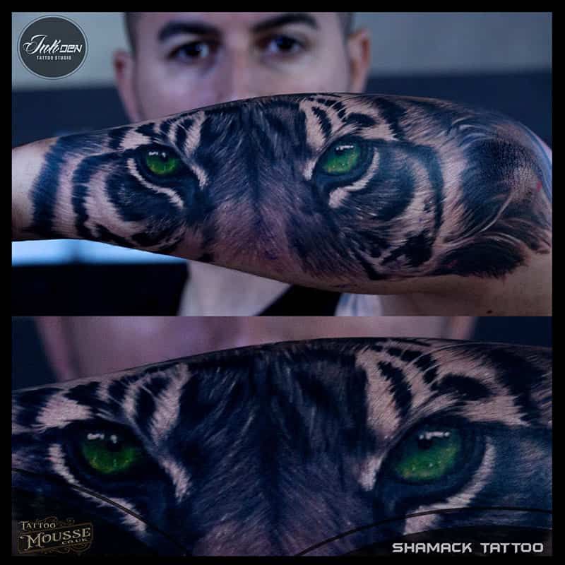 Forearm tattoo of a tiger face with green eyes, shown in two close-up views on skin