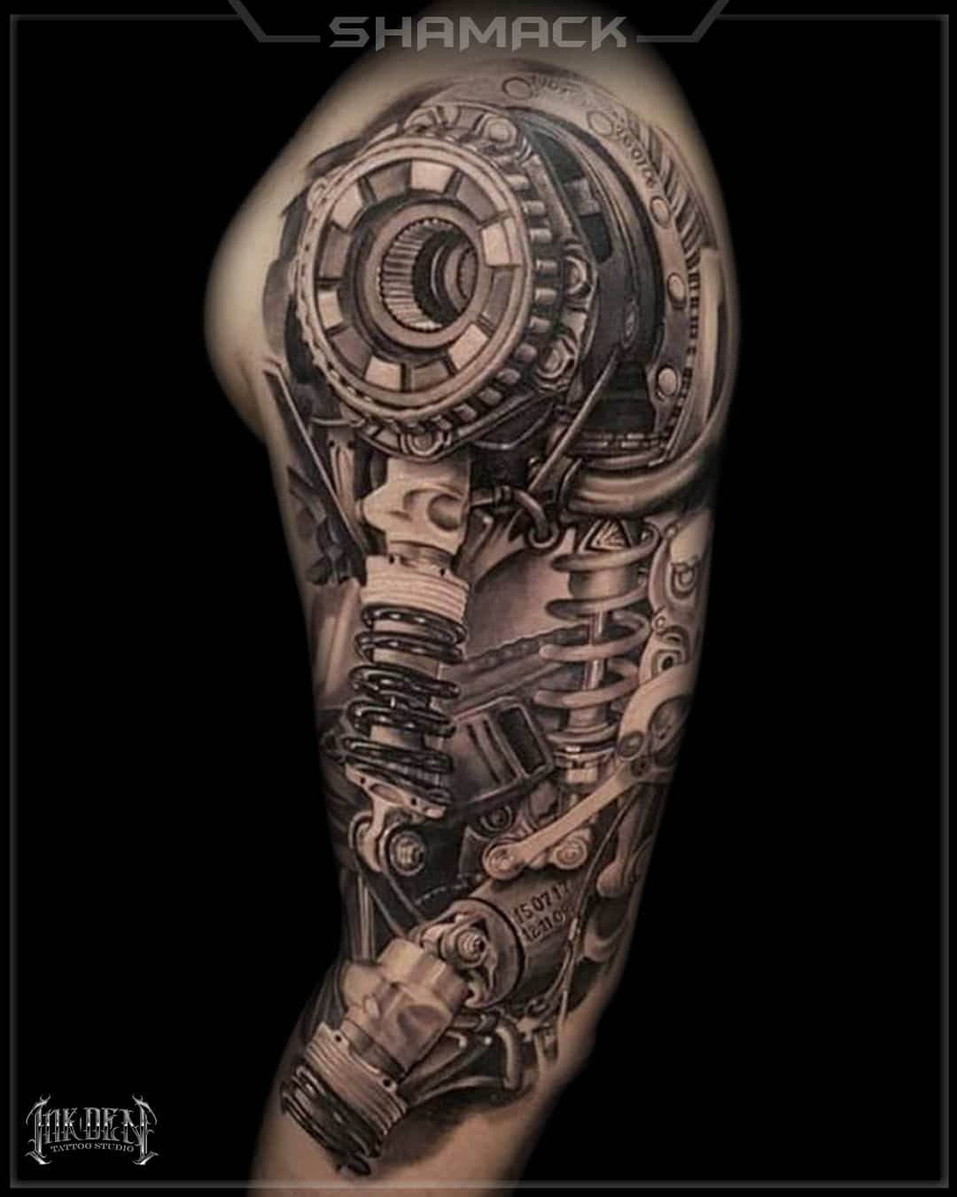 Black-and-gray biomechanical arm tattoo with gears and machinery, shown on a black background