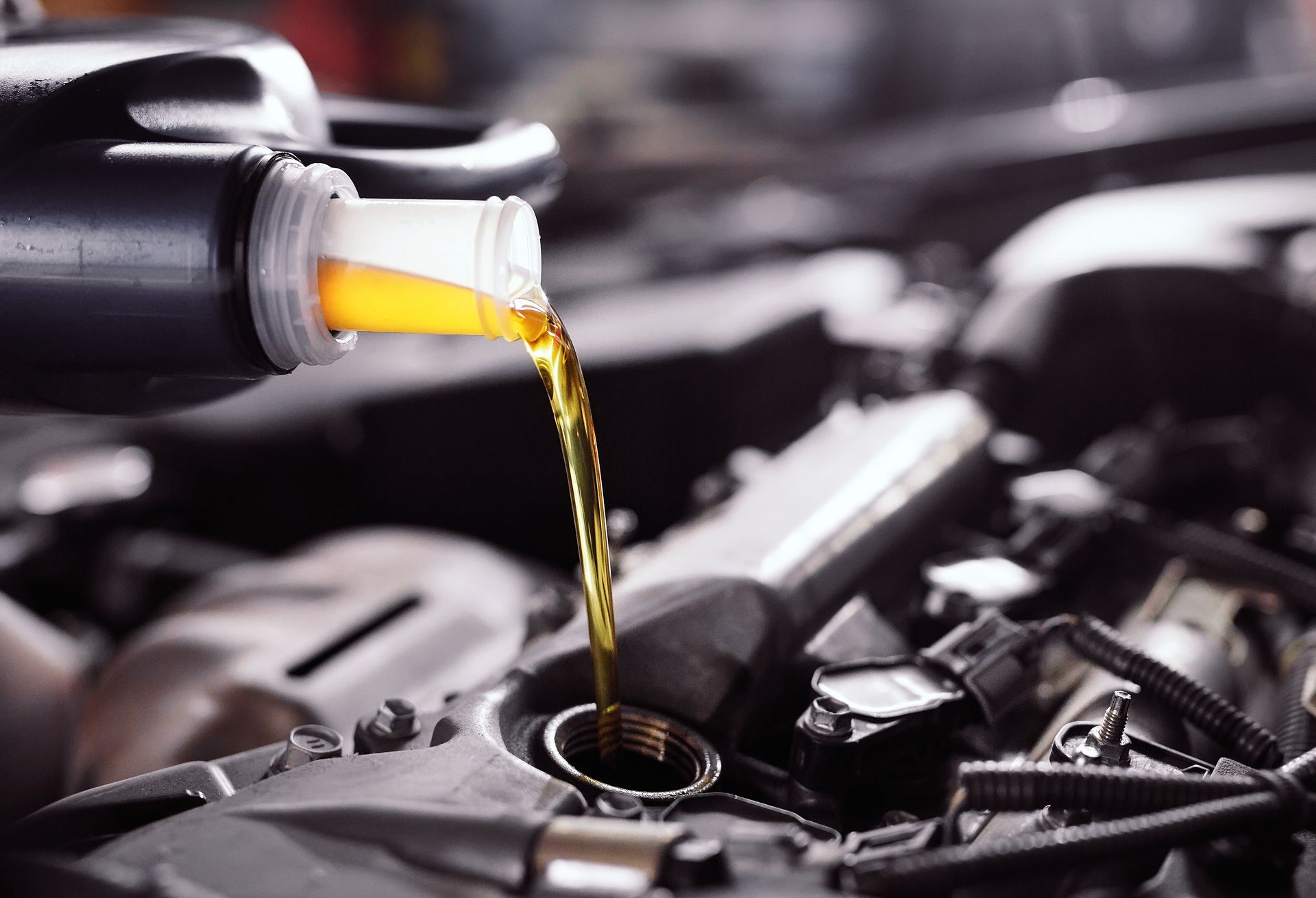 Golden engine oil pouring from a plastic bottle into an open car engine.