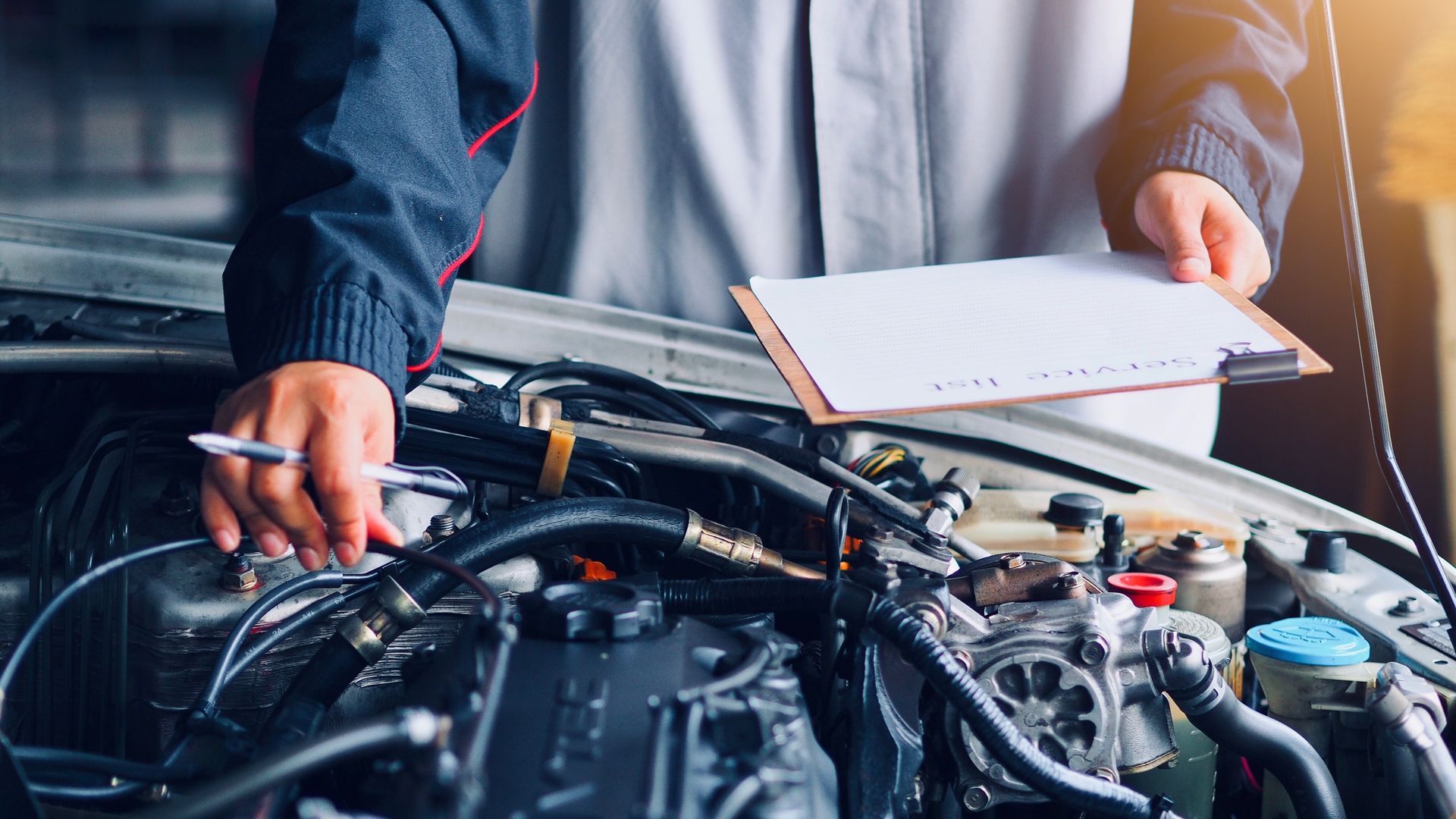A mechanic holding a pen and clipboard inspects the open engine bay of a vehicle.
