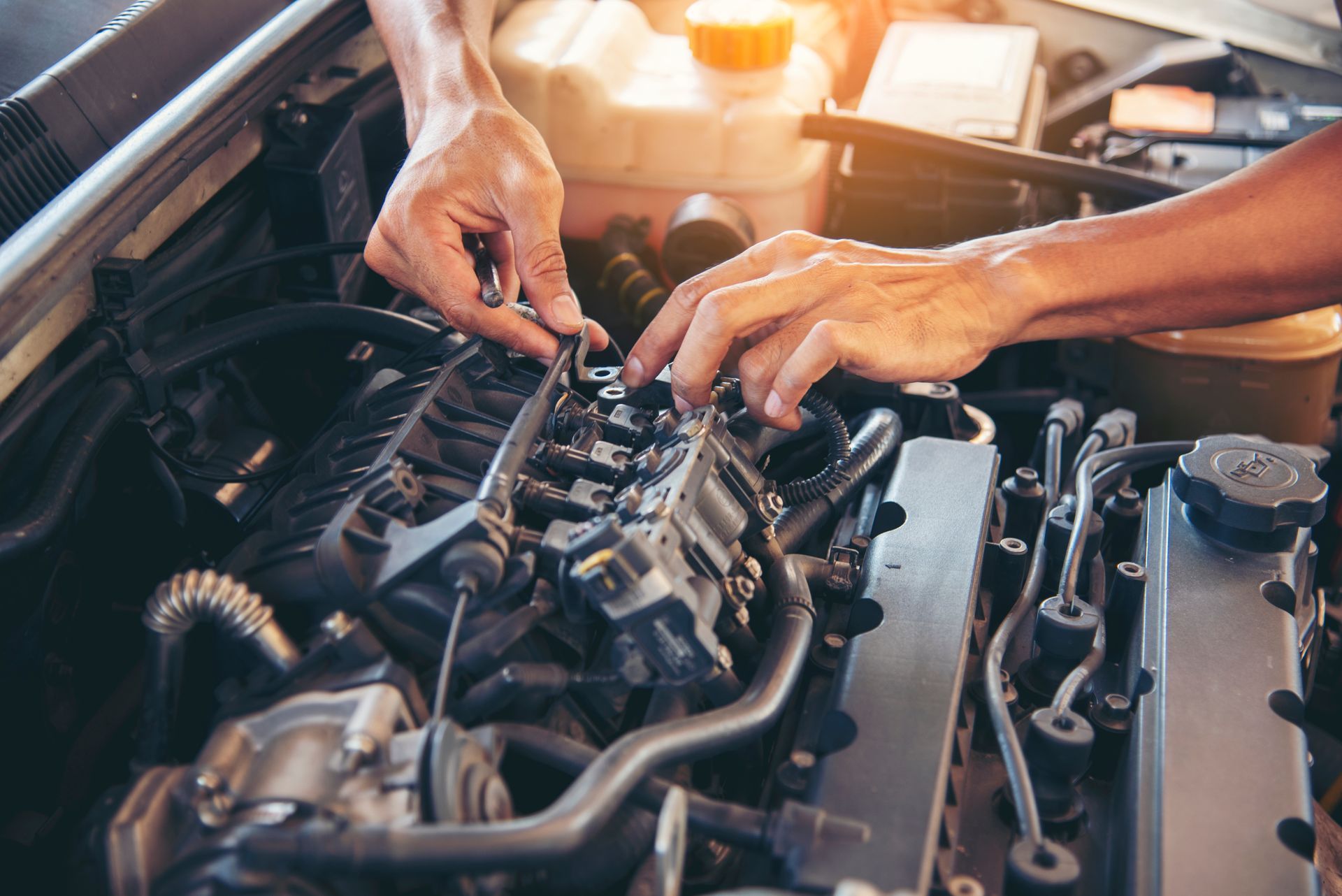 A mechanic’s hands work on the components of an open car engine in a well-lit workshop.