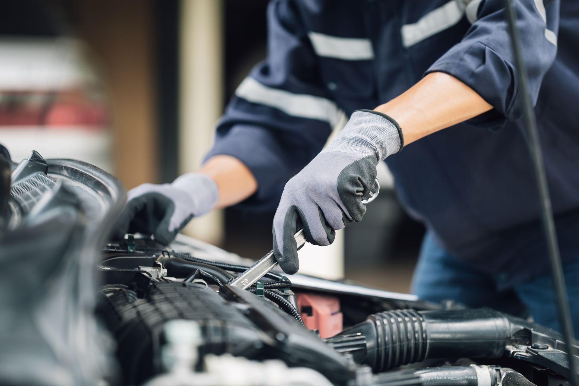 A mechanic wearing gloves works on a car engine with a wrench under the hood.