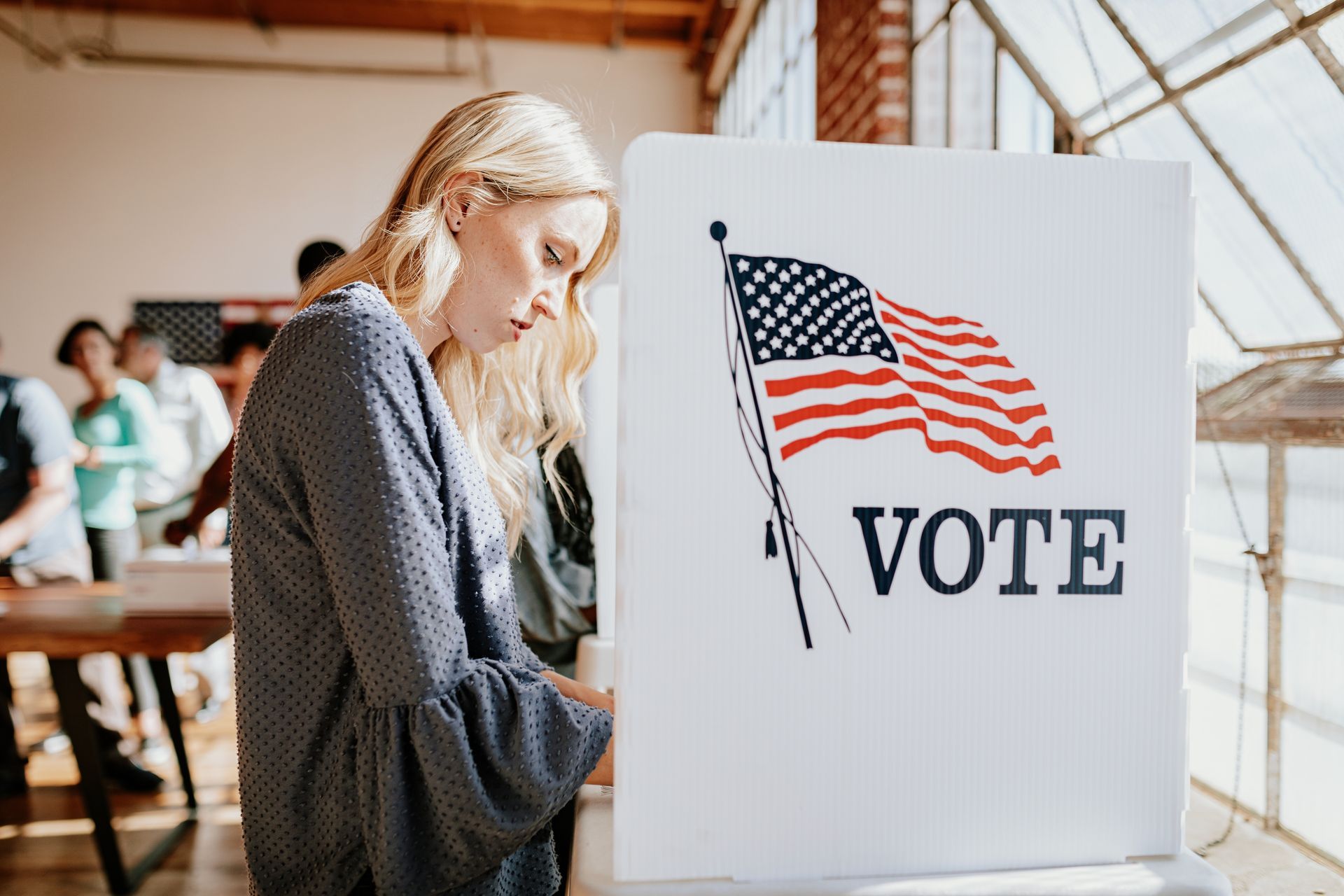 Voter marking a ballot next to a booth with U.S. flag and “VOTE” sign