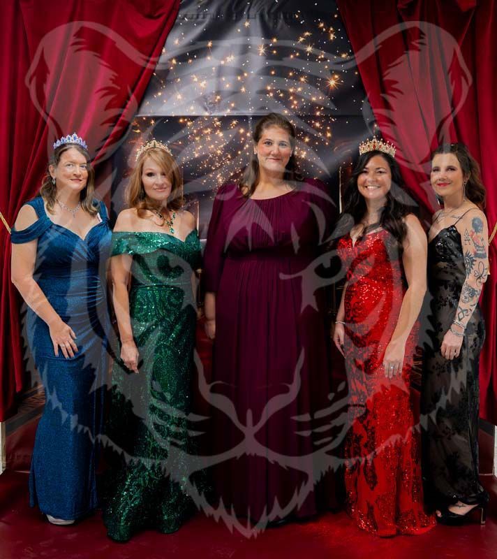 Five people in formal evening gowns stand in a row before a backdrop with red curtains and twinkling lights.