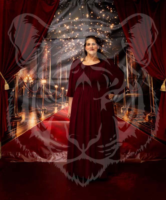 A person in a long maroon dress stands on a red carpet in front of a draped backdrop, overlaid with a faint tiger outline.