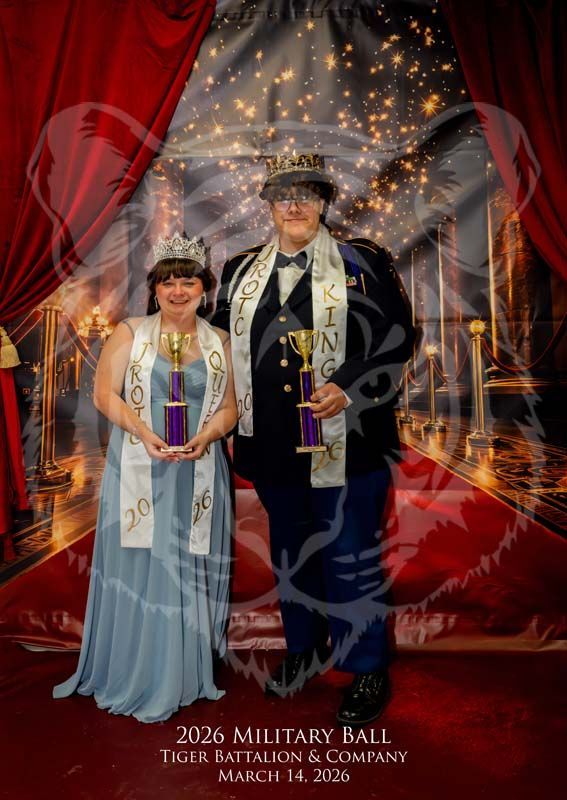 Two people in formal attire stand on a red carpet at the 2026 Military Ball, holding trophies and wearing pageant sashes.