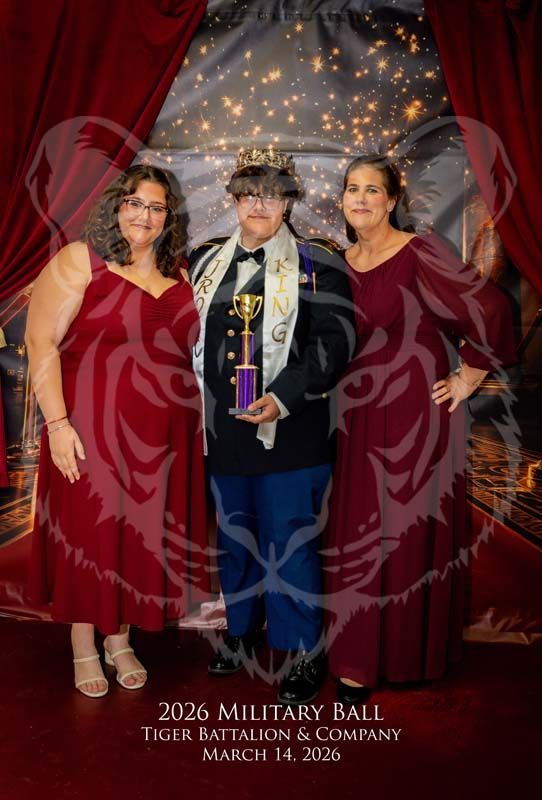 Three people pose for a photo at a military ball; the center person holds a trophy, flanked by two people in red dresses.