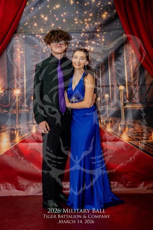 A couple stands together for a formal photo at the 2026 Tiger Battalion Military Ball in front of a red-curtained backdrop.