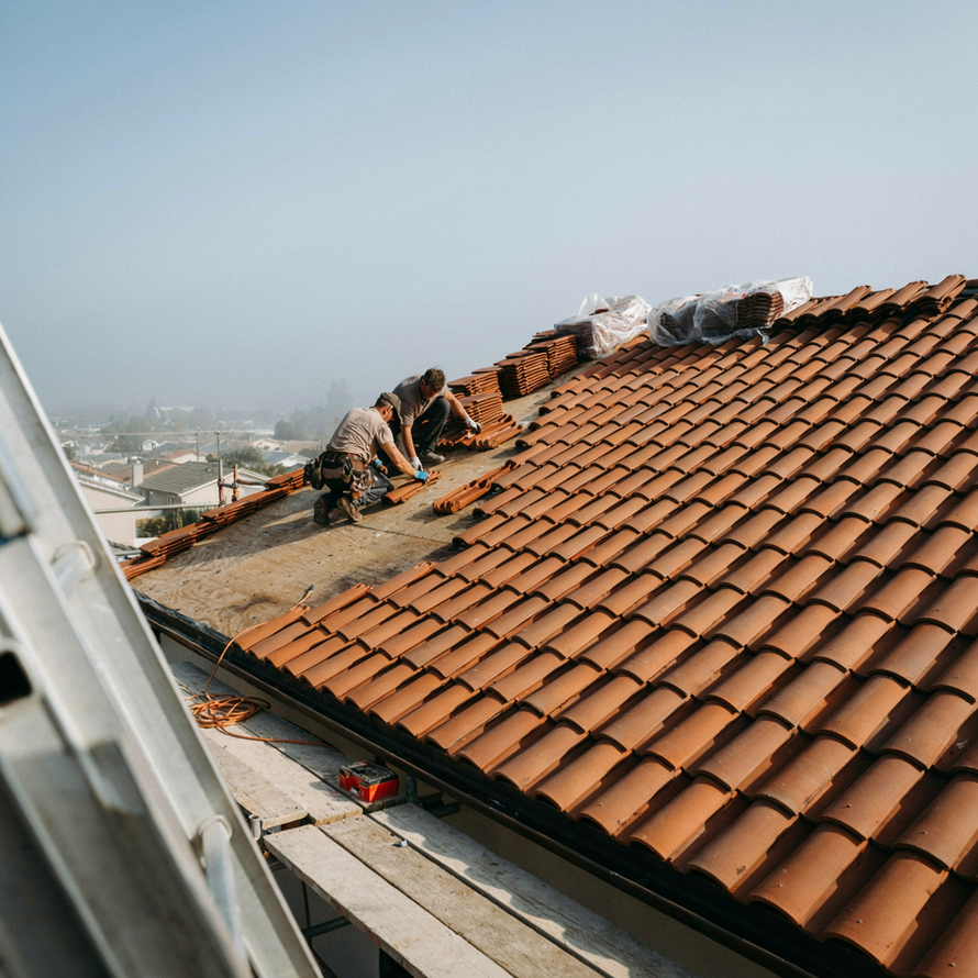 Workers repairing terracotta roof tiles on a house rooftop