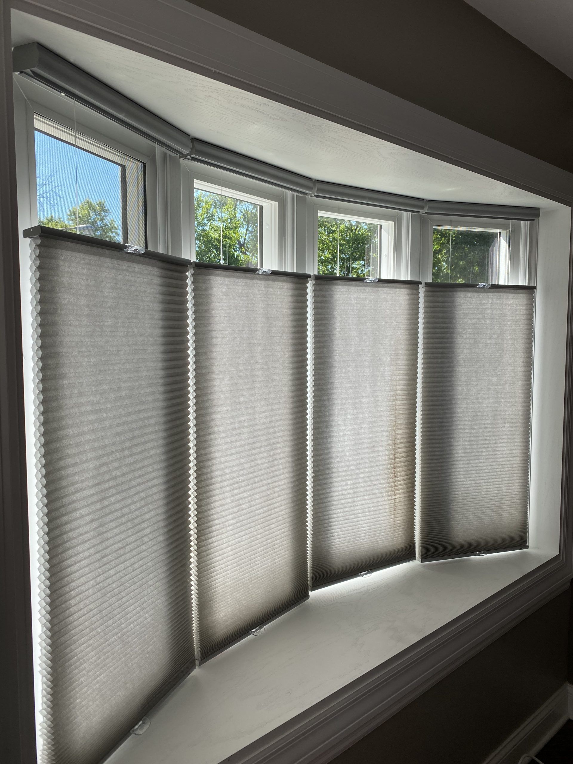 Closed gray cellular shades on a bay window with sunlight filtering through.