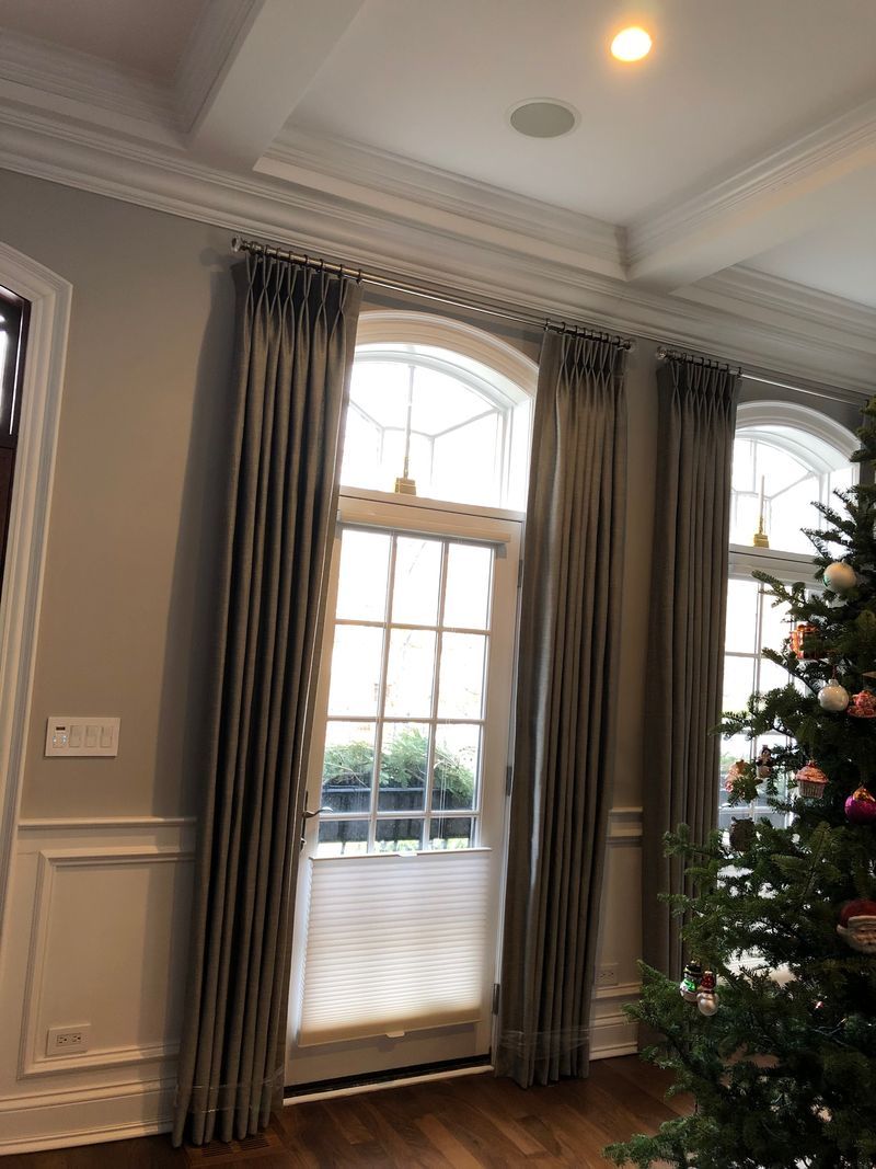 Living room with tall arched windows, gray curtains, and a decorated Christmas tree.