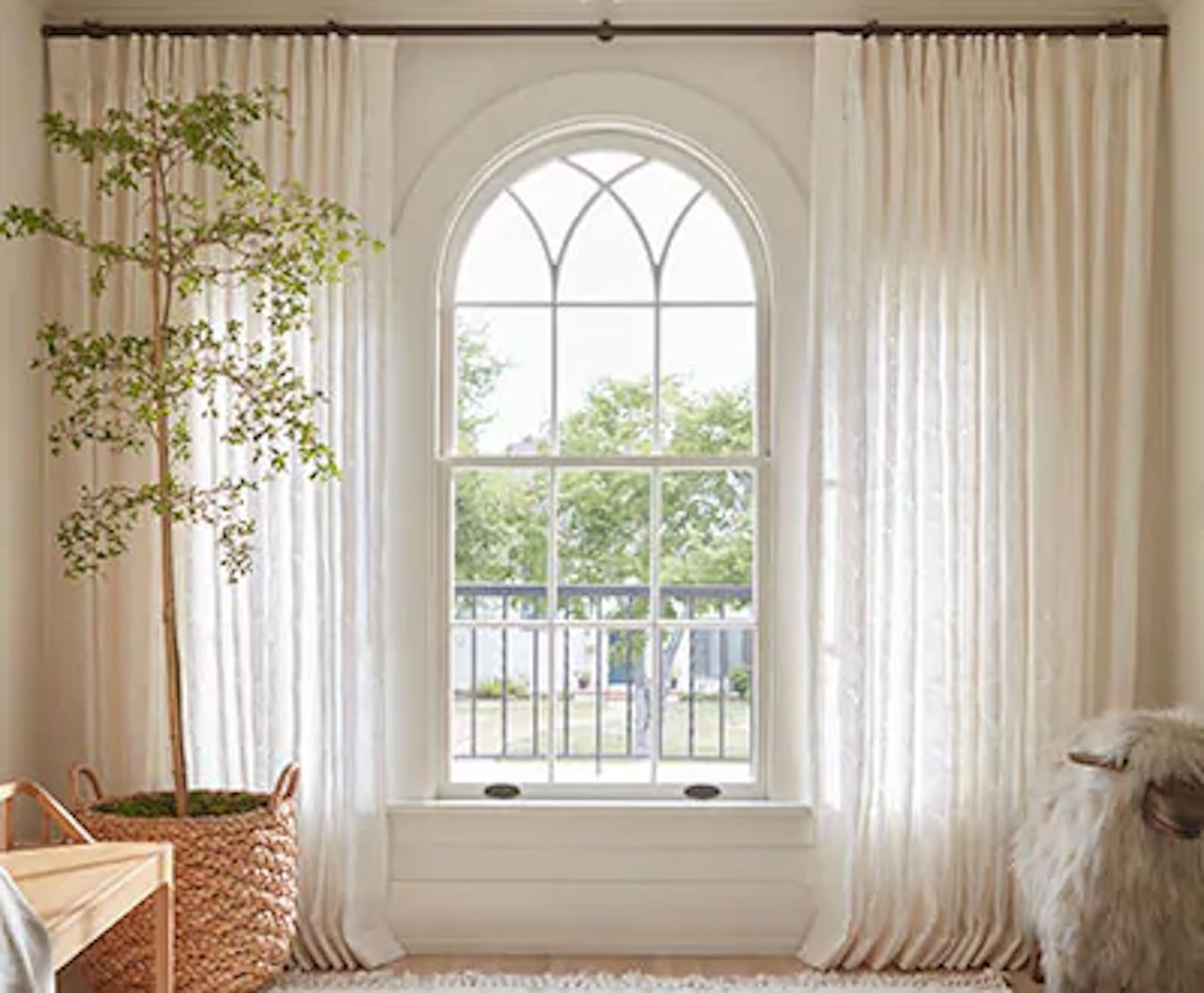 Bright room with arched window, sheer curtains, potted tree, and a woven basket