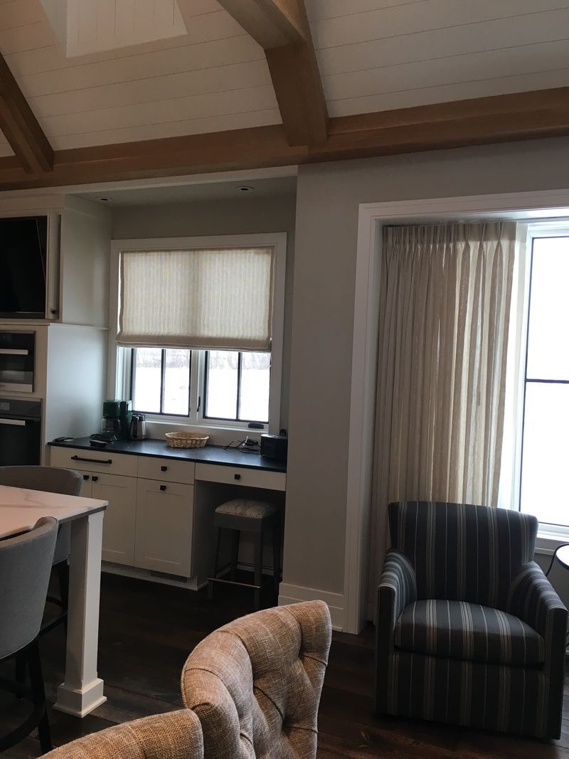 Cozy living room with high wooden beams, kitchen pass-through, striped armchair, and window blinds.