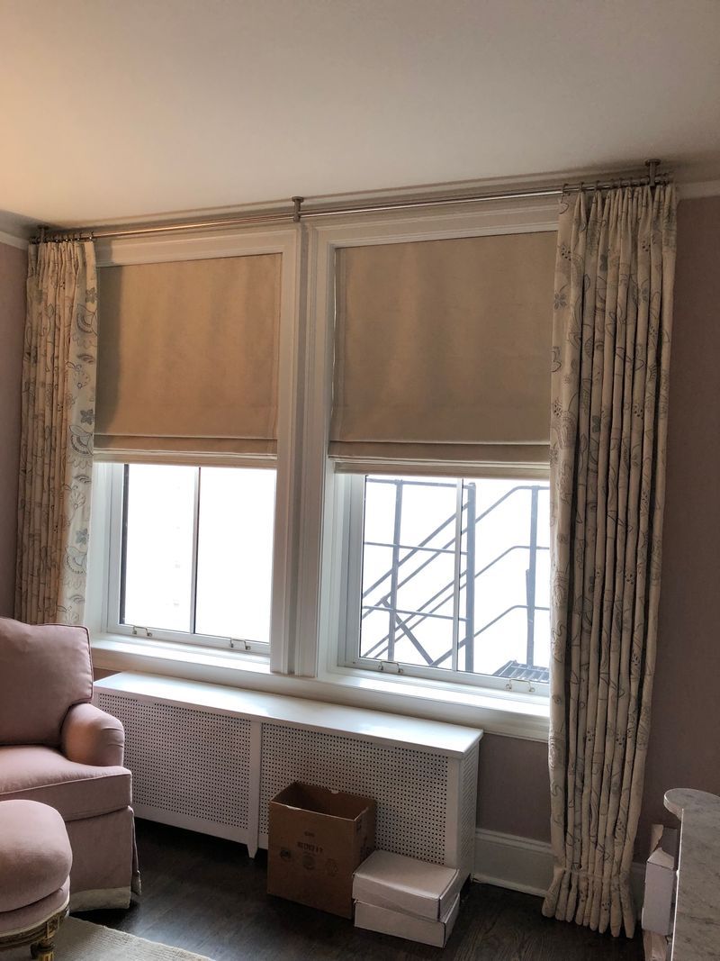 Living room with beige blinds, patterned curtains, pink chair, and radiator under a window