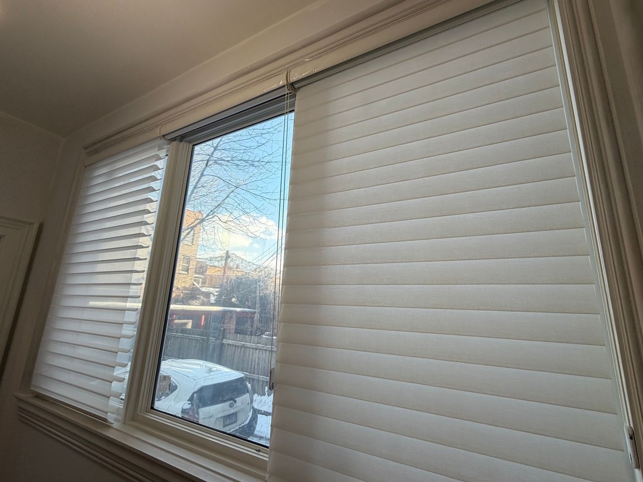 White window blinds partially open, showing a snowy street and blue sky outside.