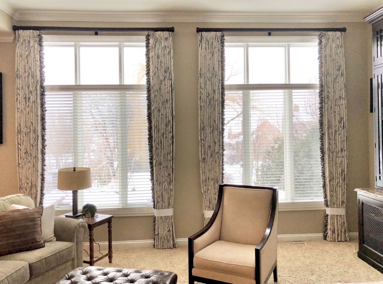 Bright living room with large windows, beige chair, side table, and patterned curtains