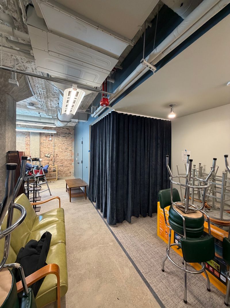 Industrial interior with black curtains, brick wall, chairs, and stacked metal stools under exposed ductwork