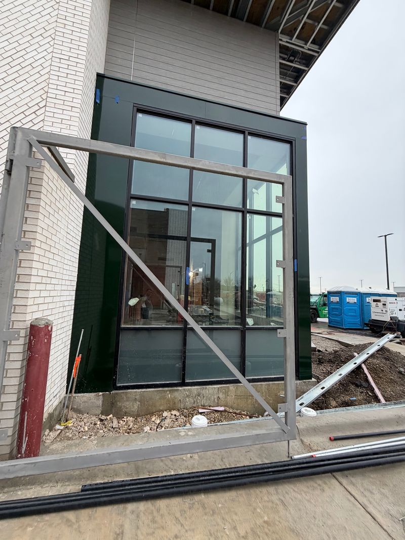 Partially installed glass storefront entrance at a construction site, with metal framing and debris nearby