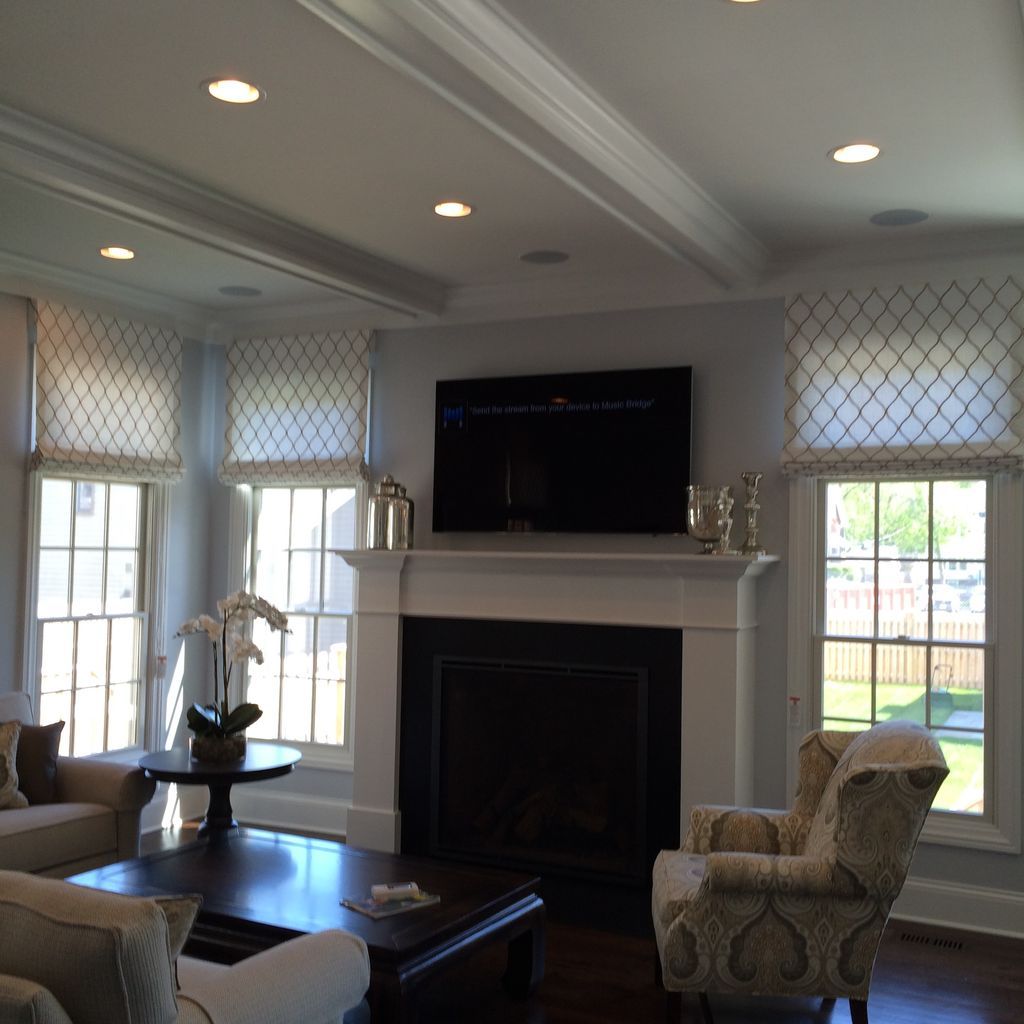 Bright living room with fireplace, wall-mounted TV, tall windows, and patterned chairs around a coffee table