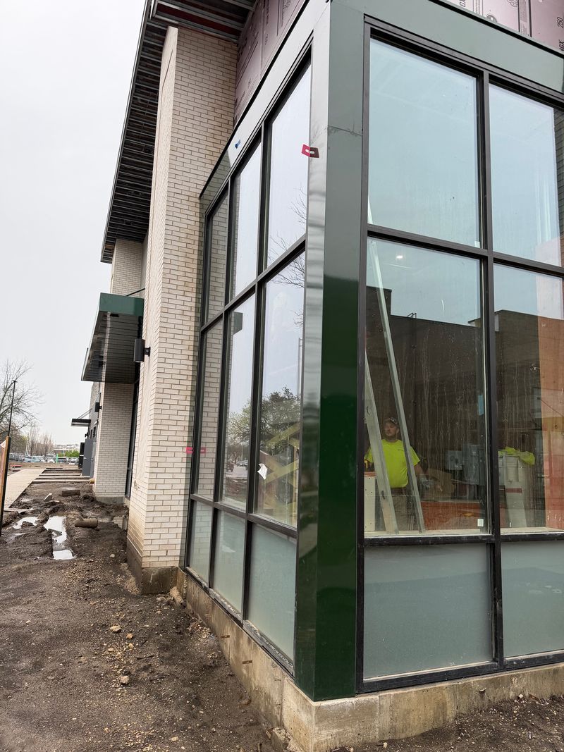 Glass-walled extension on a house with dark green trim, shown from the side on a muddy construction site