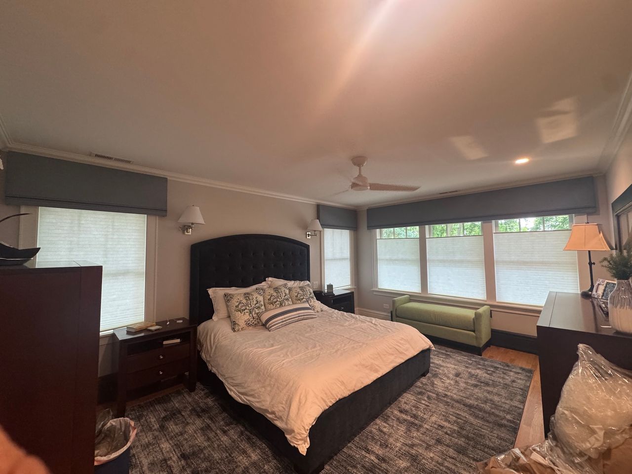 Spacious bedroom with a large bed, windows, green loveseat, and dark dresser under soft ceiling light