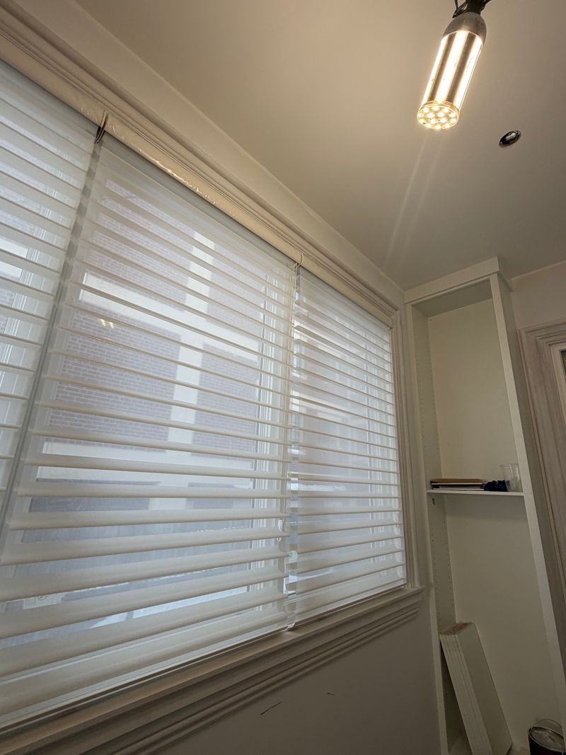 Bright white window blinds in a corner room with a ceiling light and built-in shelves.