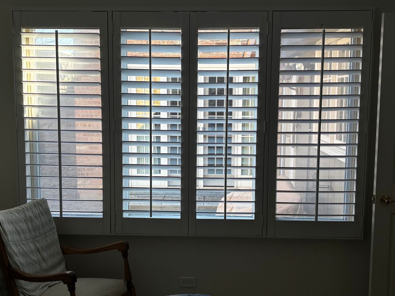 Living room window with white shutters, showing an apartment building outside