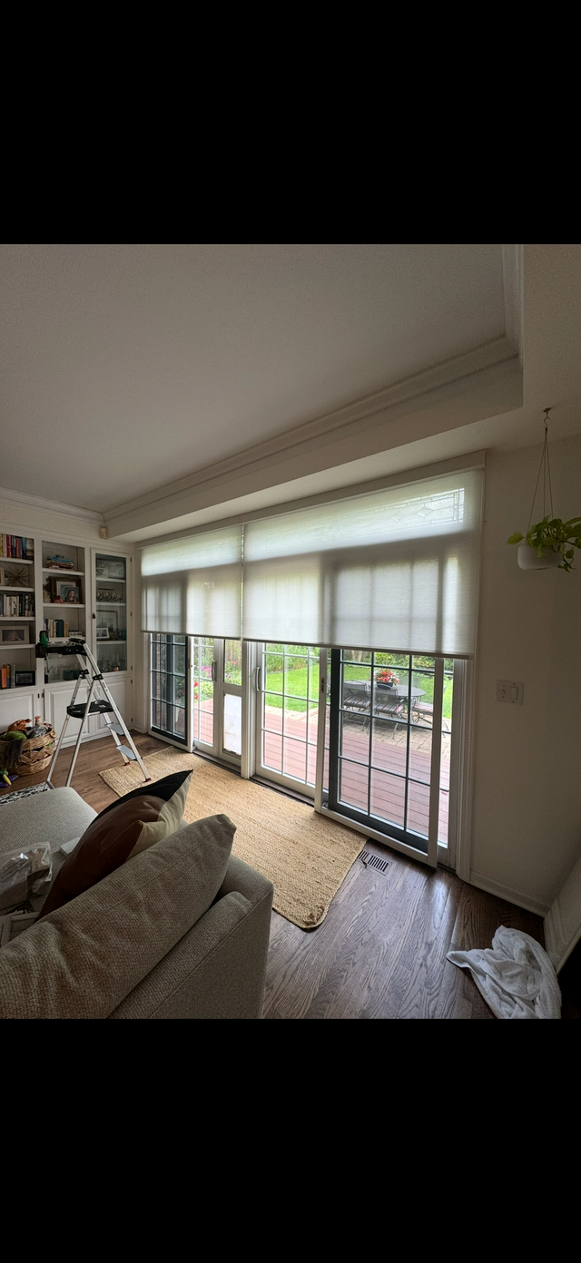 Bright living room with large windows, sofa, shelves, and balcony doors letting in natural light.