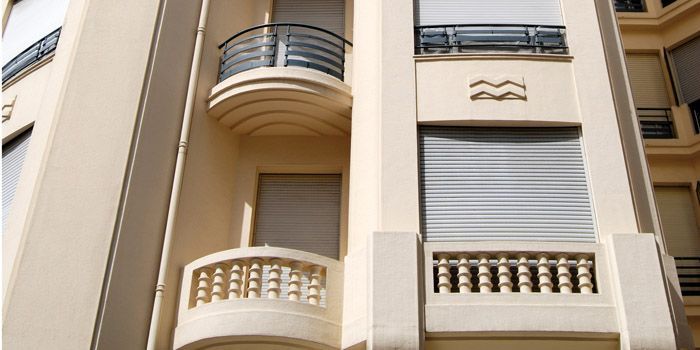 Exterior of a beige apartment building with balconies and closed white shutters