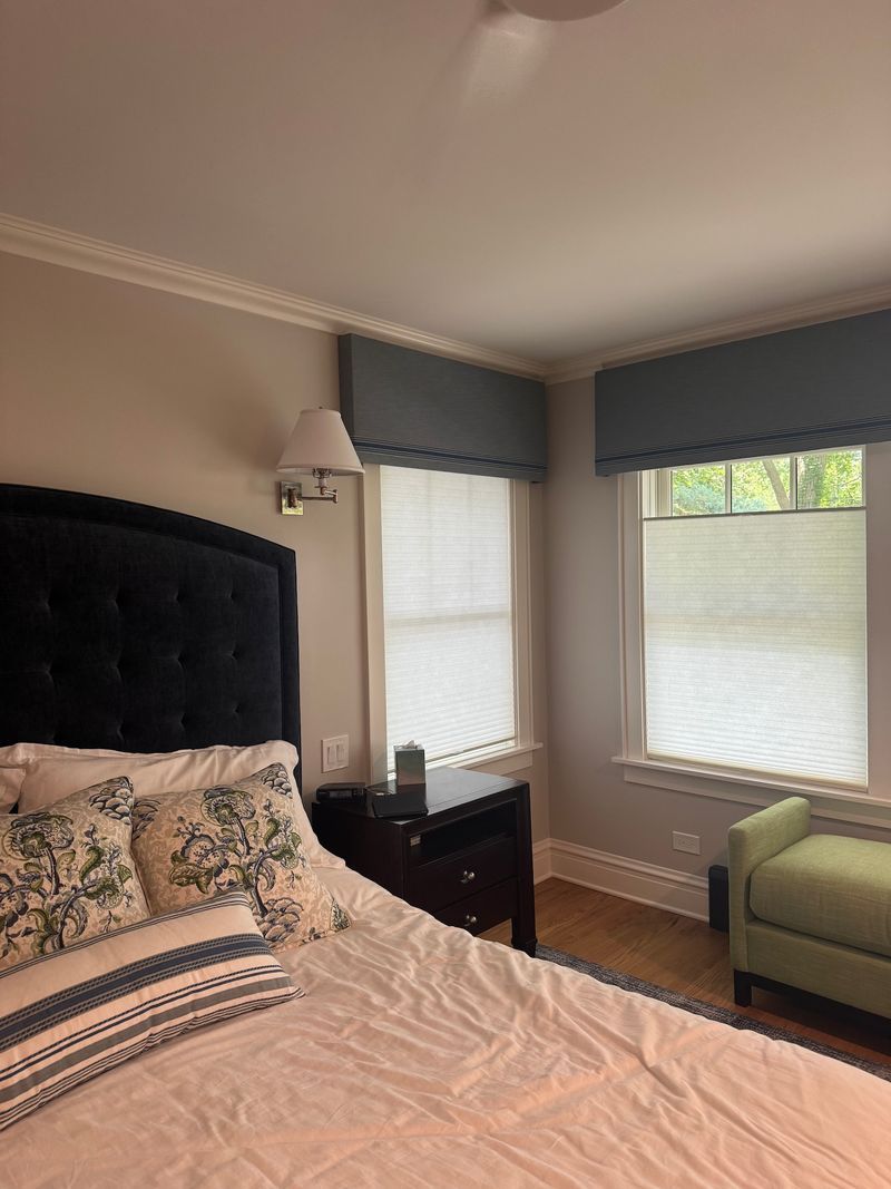 Bedroom with a black tufted headboard, light bedding, gray walls, two windows, and a green chair.