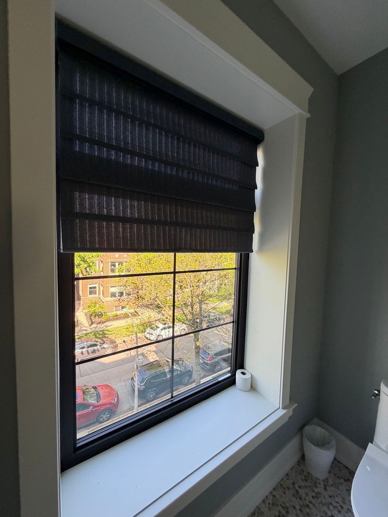 Window with black blinds partially open, showing a street view and white windowsill in a gray room.