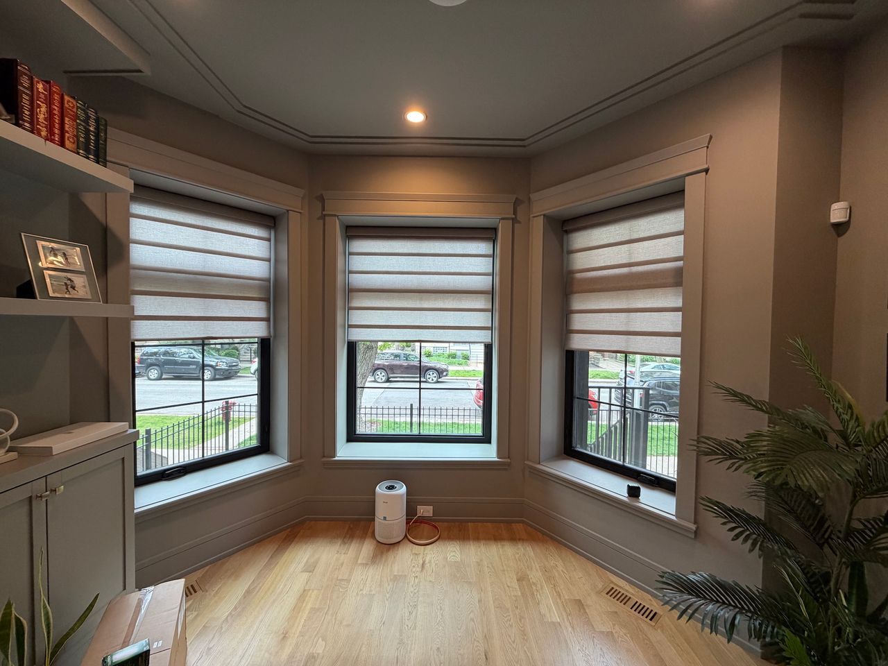 Empty sunlit room with bay windows, light wood floor, and a small plant by the wall.