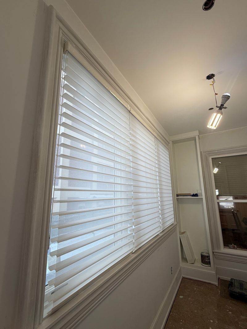 Bright hallway with white window blinds, trim, and a wall mirror under ceiling lights.