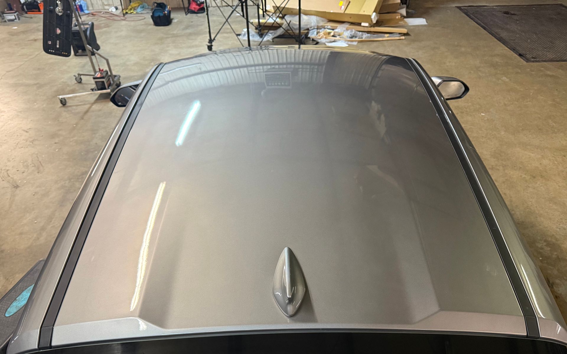 High-angle view of a metallic silver car roof featuring a shark fin antenna in a garage setting.
